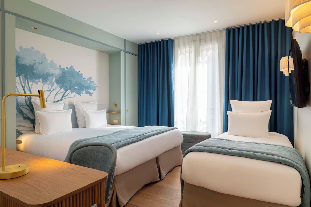 A hotel room with two beds, a desk, a chair, a lamp, and a painting on the wall.
