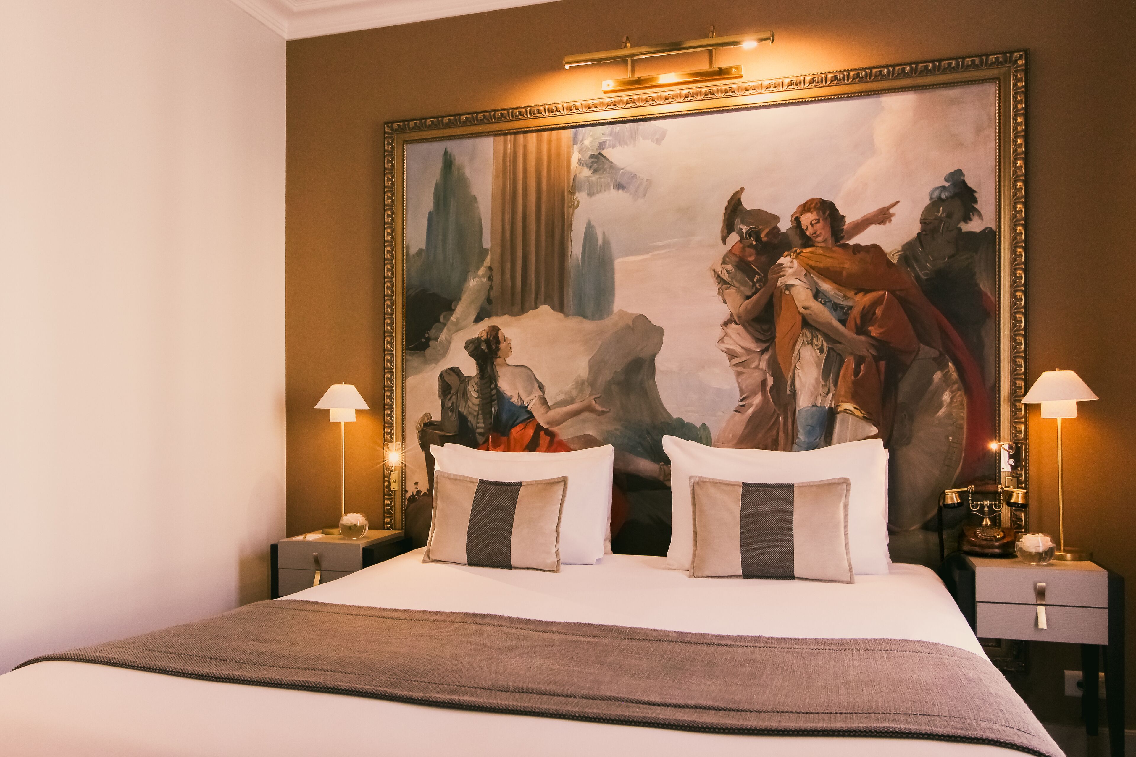 A hotel room with a large bed, two bedside tables with lamps, and a large framed painting on the wall.