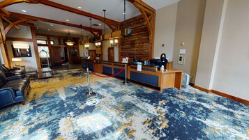 Eine Lobby mit einer Rezeption, Holzbalken, einem gemusterten Teppich und einer Sitzecke mit Ledersofas.