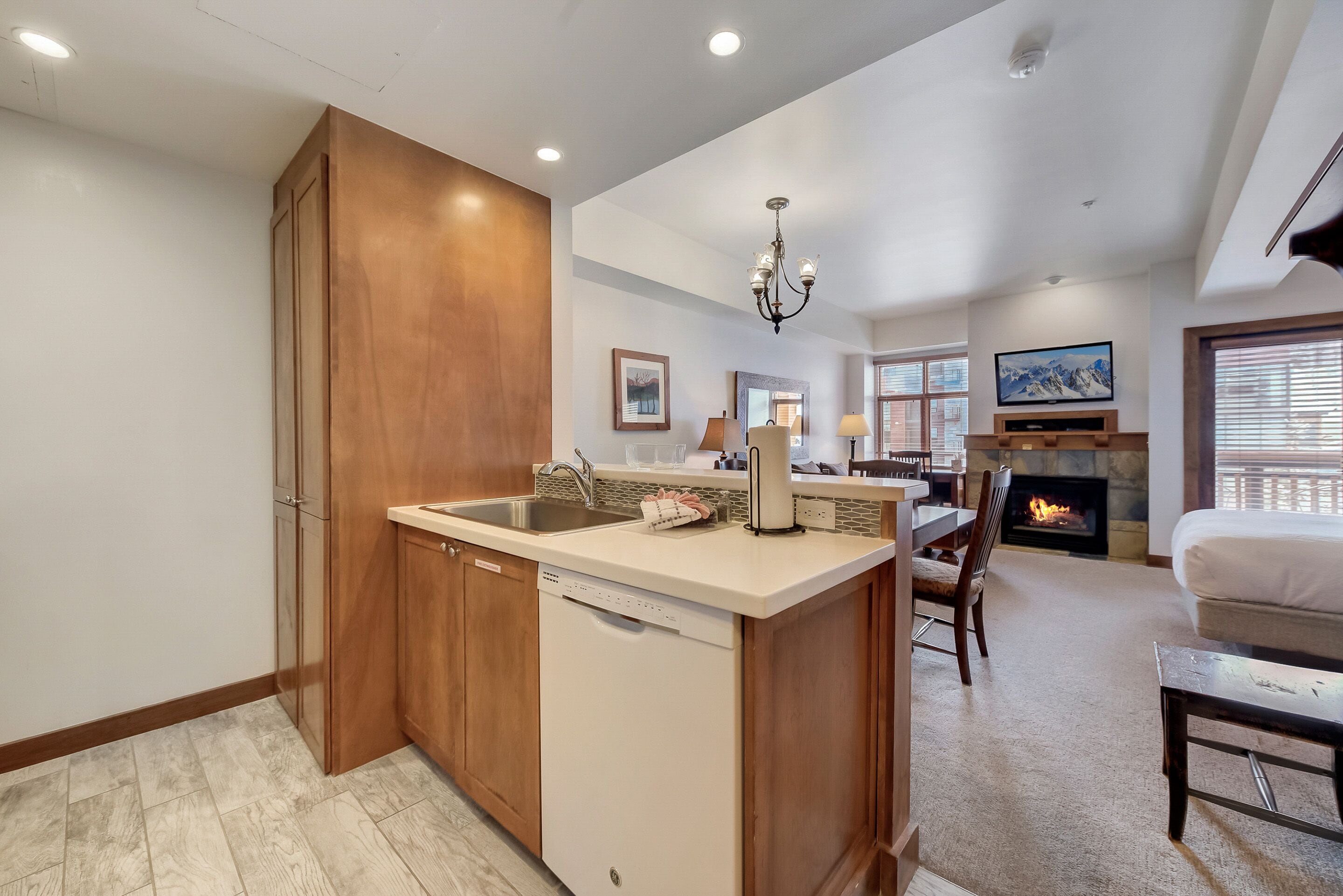 A modern kitchen with wooden cabinets, a dishwasher, and a dining area with a fireplace.