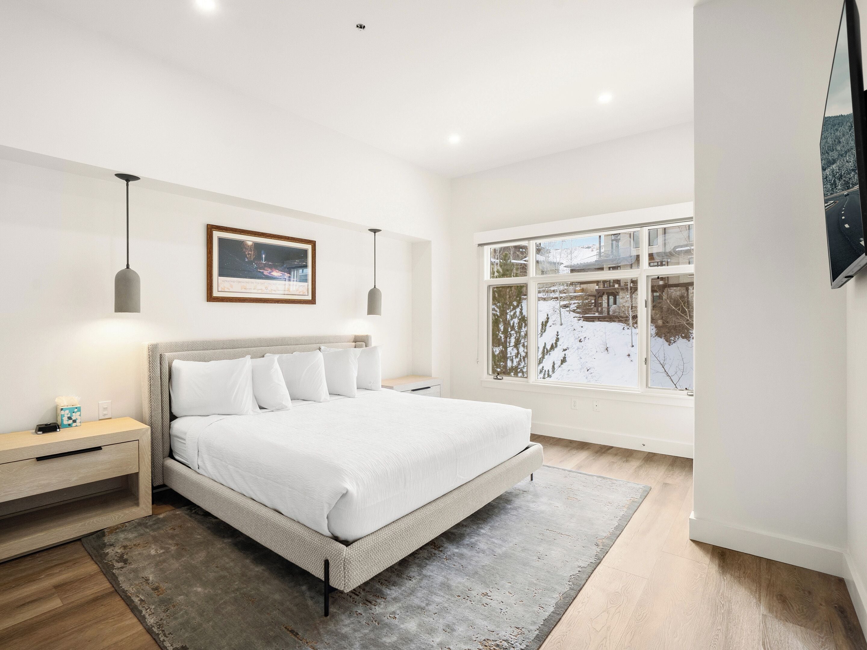 Ein modernes Schlafzimmer mit einem großen Bett, Nachttischen, einem Teppich und einem Fenster mit Blick auf Schnee.