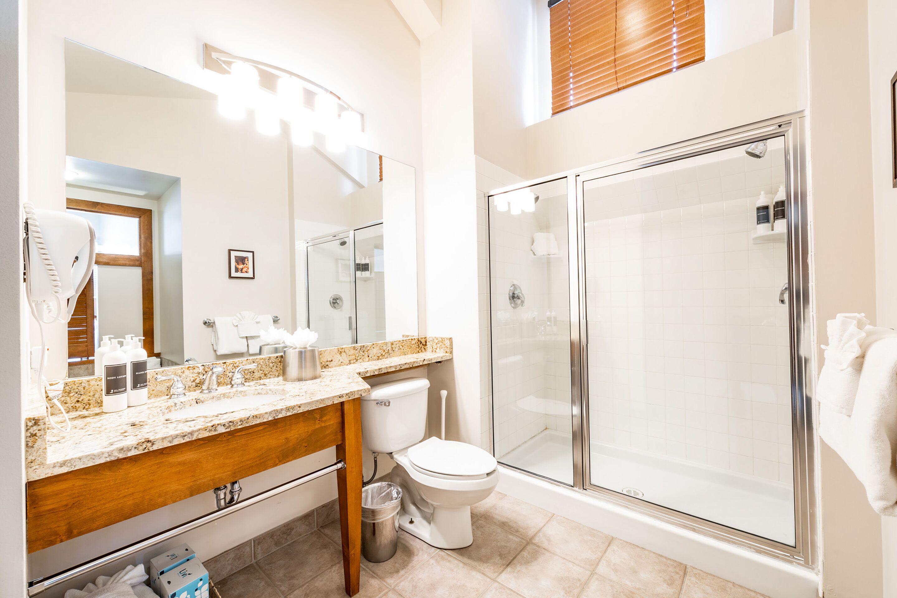 A modern bathroom with a granite countertop, a toilet, a glass-enclosed shower, and a large mirror.