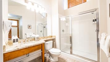A modern bathroom with a granite countertop, a toilet, a glass-enclosed shower, and a large mirror.
