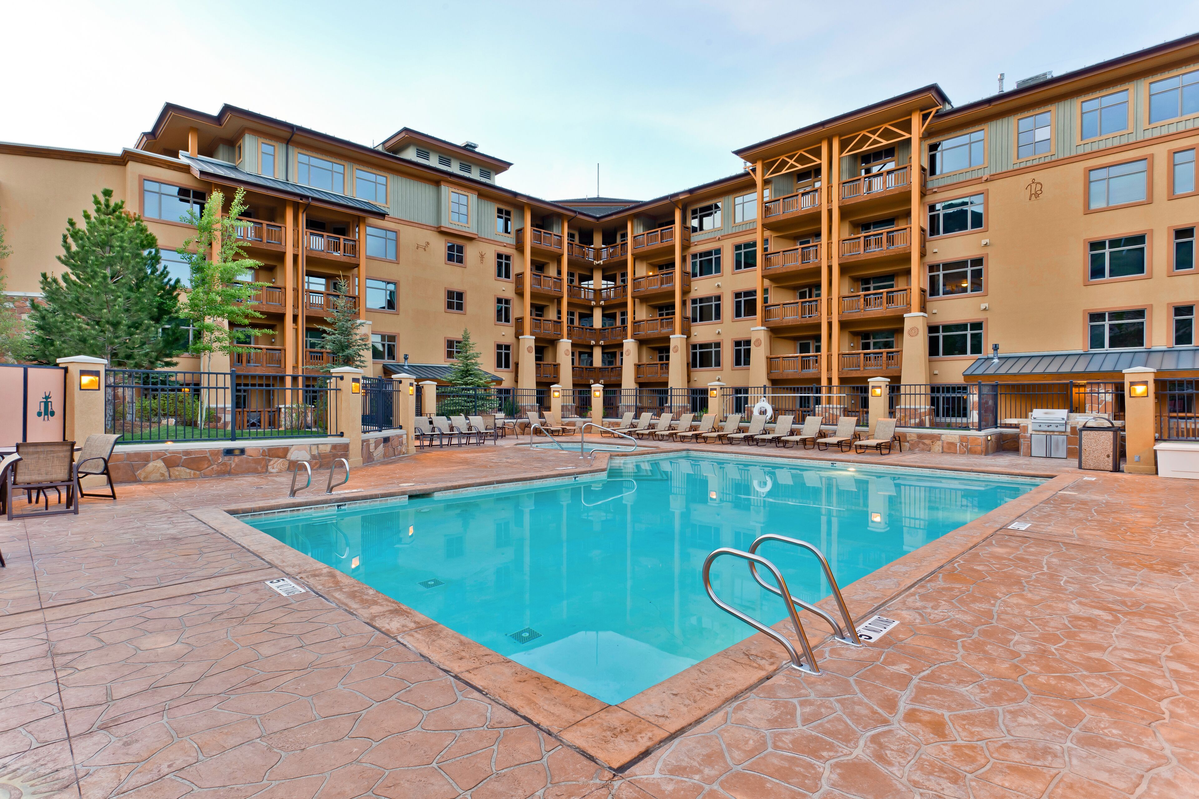 A pool area with lounge chairs and a clear blue pool, surrounded by multi-story buildings with balconies.
