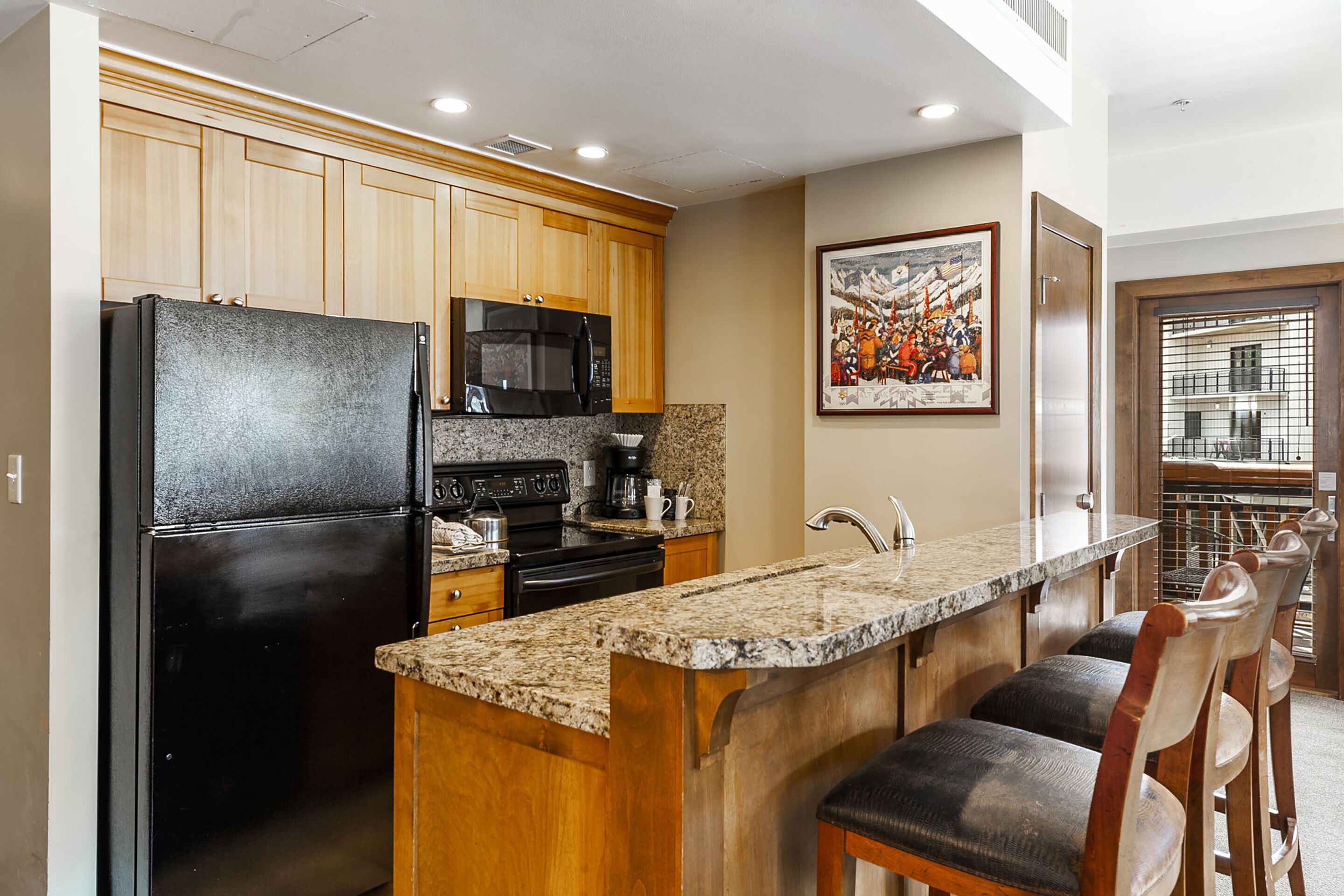 A kitchen with wooden cabinets, a black refrigerator, a microwave, and a granite countertop.