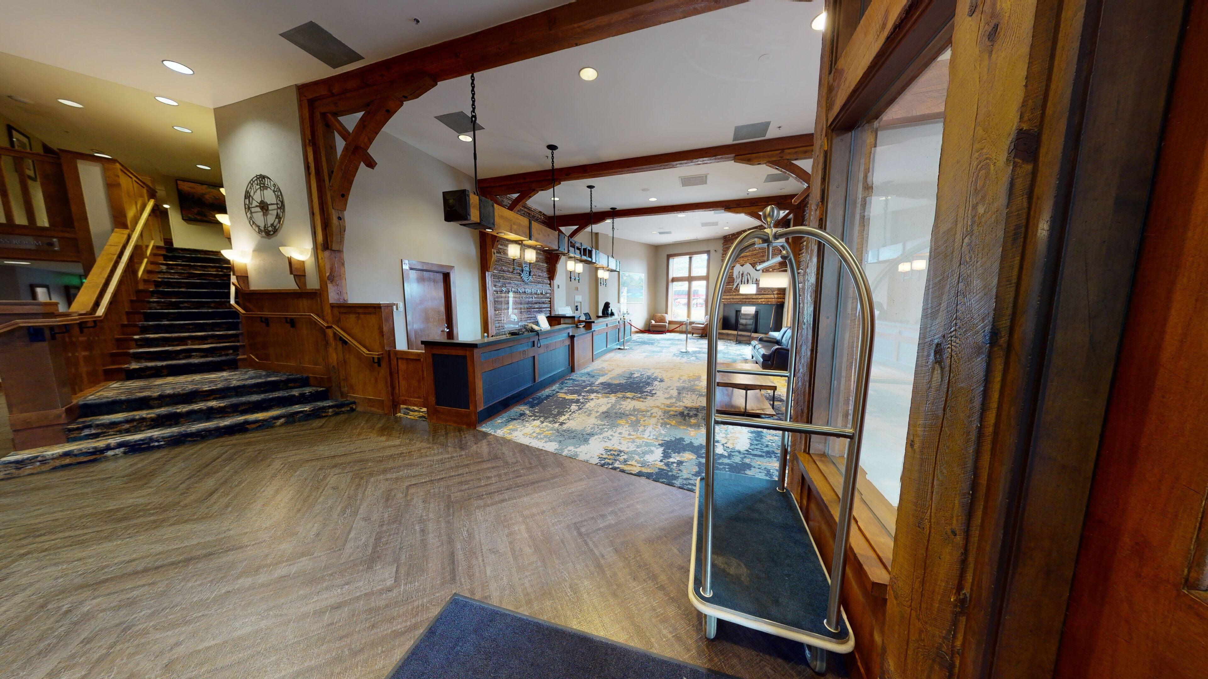 A spacious lobby with a wooden staircase, a reception desk, and a seating area with a view of the outside.
