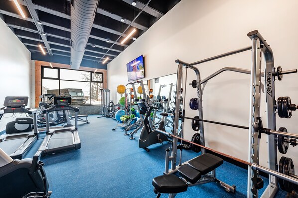 A gym with treadmills, weight machines, and a TV on the wall.