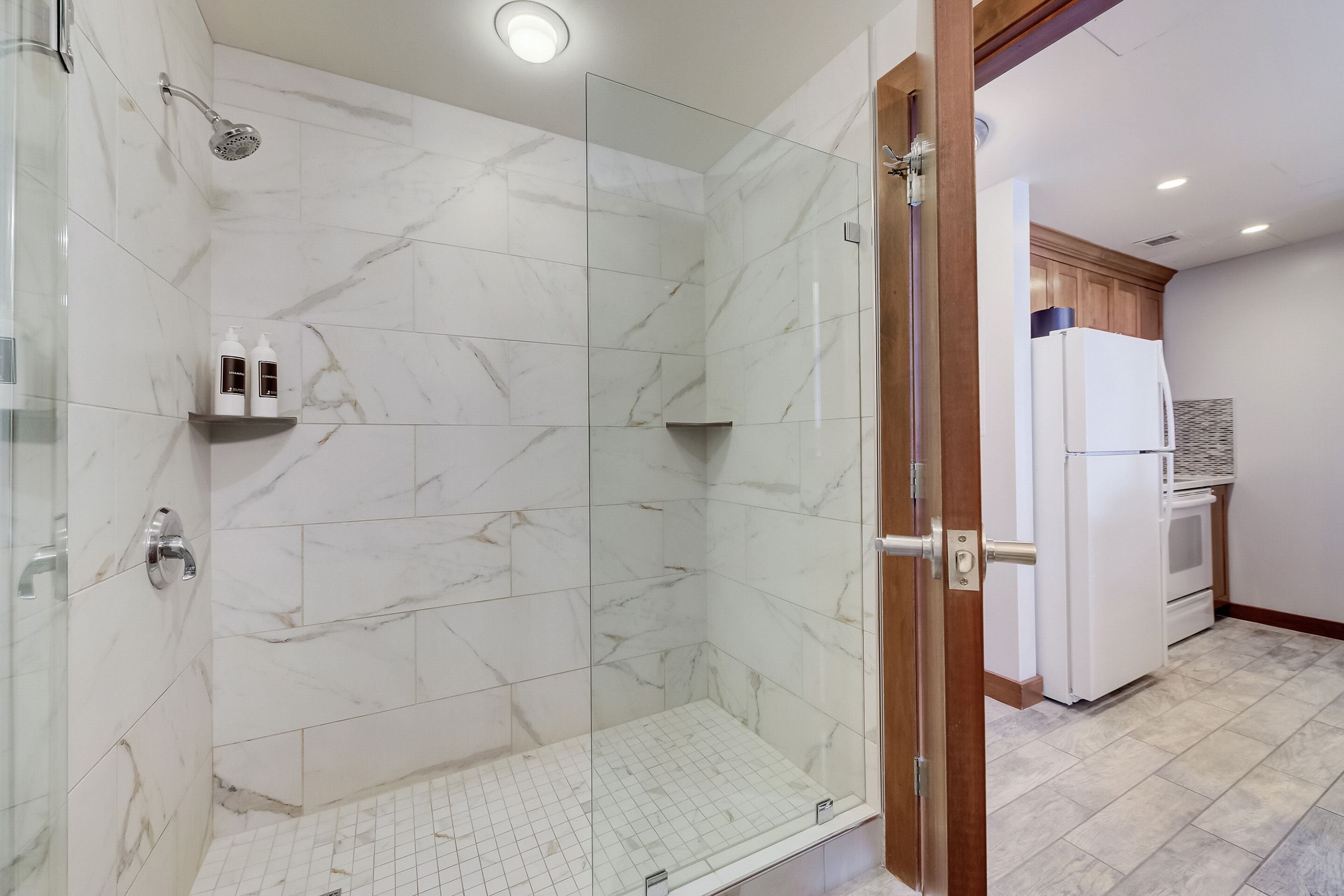 Un baño moderno con cabina de ducha de vidrio, baldosas de mármol y estante empotrado con artículos de aseo.