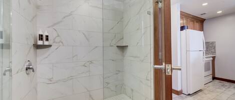 Un baño moderno con cabina de ducha de vidrio, baldosas de mármol y estante empotrado con artículos de aseo.
