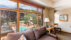 Ein Zimmer mit großem Fenster, einer Couch, einem Tisch mit Lampe und einem gerahmten Bild an der Wand.