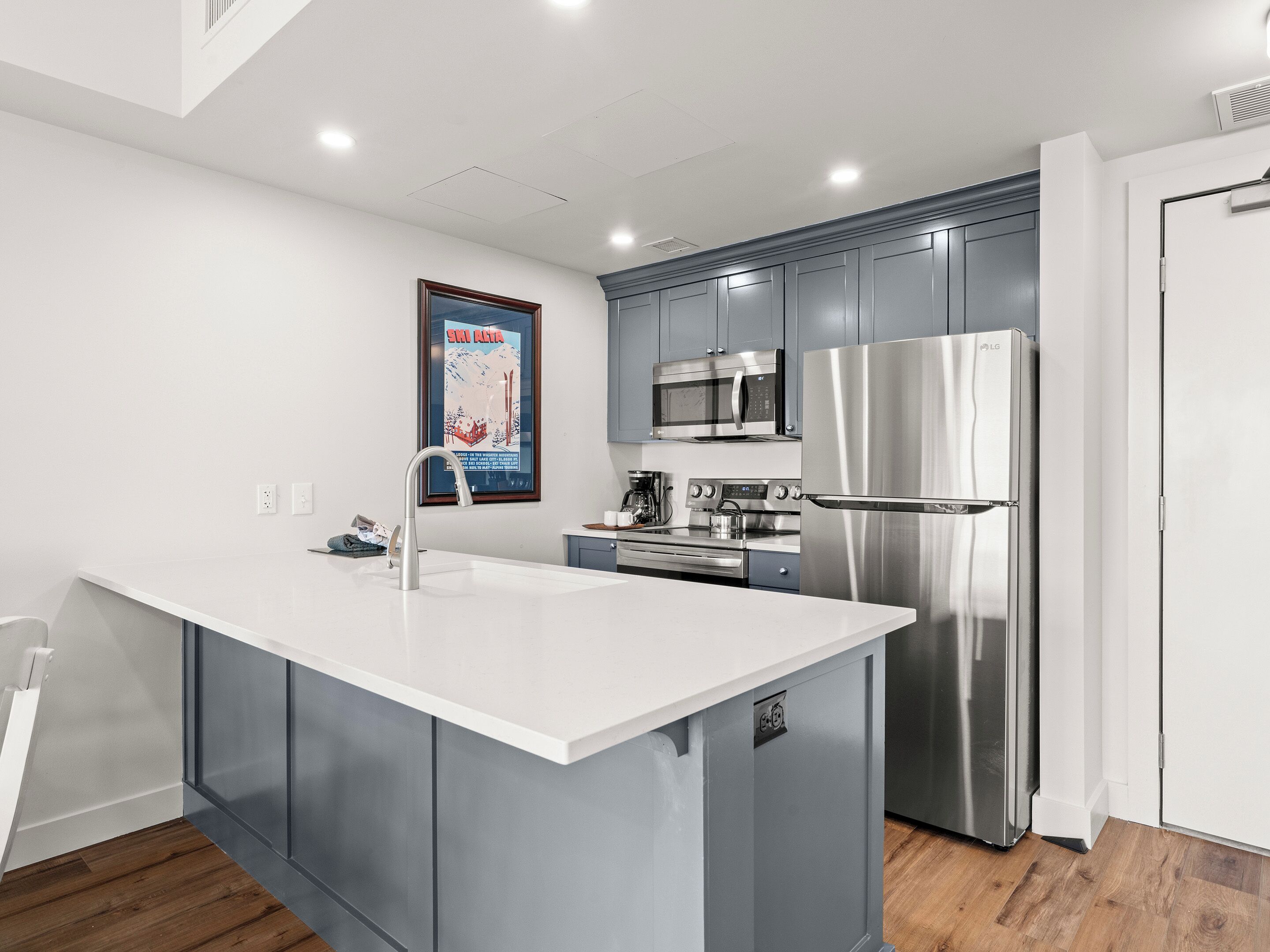 A modern kitchen with grey cabinets, a stainless steel refrigerator, a microwave, and an island with a sink.