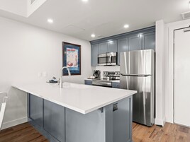 Una cocina moderna con armarios grises, un refrigerador de acero inoxidable, un microondas y una isla con un fregadero.