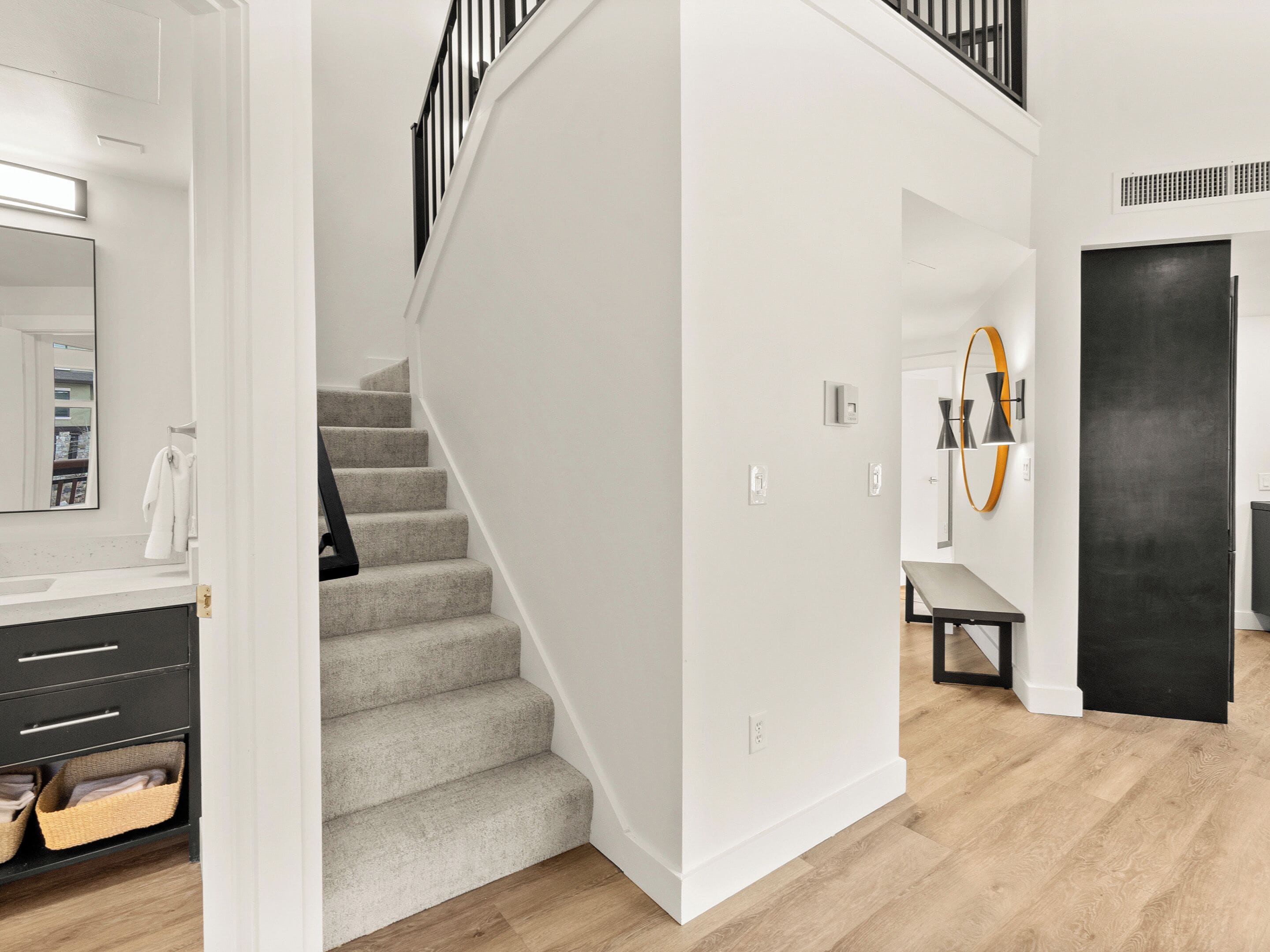 A modern interior with a staircase, a bathroom with a mirror, and a dining area with a bench.