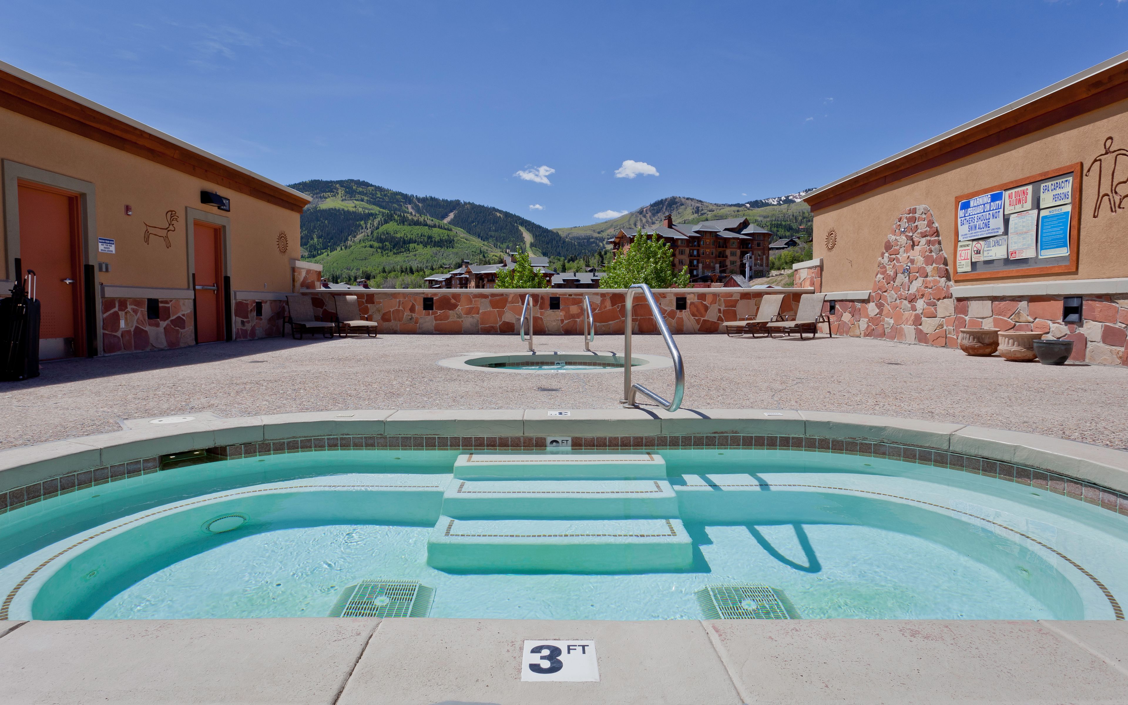 A pool area with a 3 FT depth marker, lounge chairs, and a view of mountains.