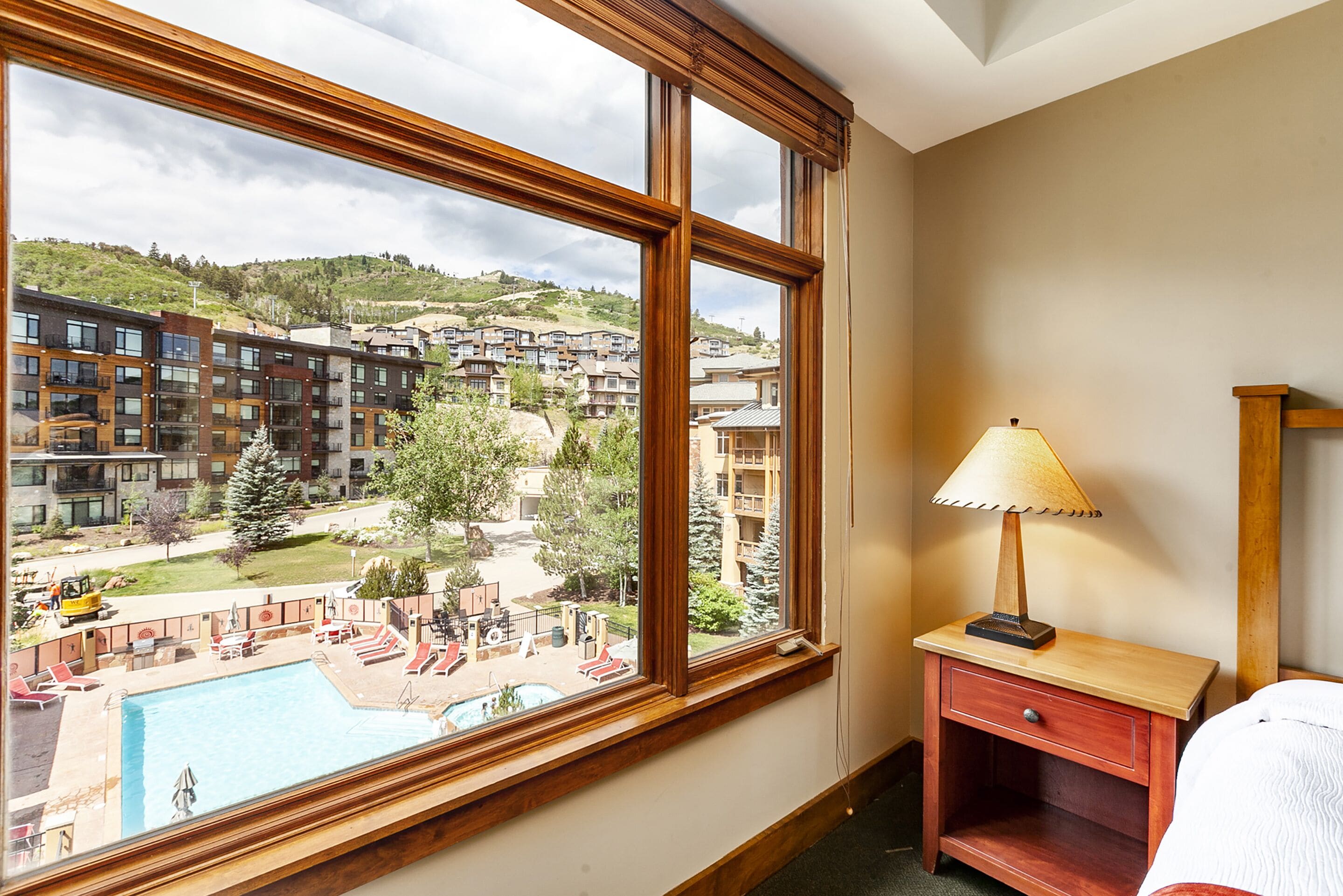A hotel room with a large window overlooking a pool and a view of surrounding buildings.