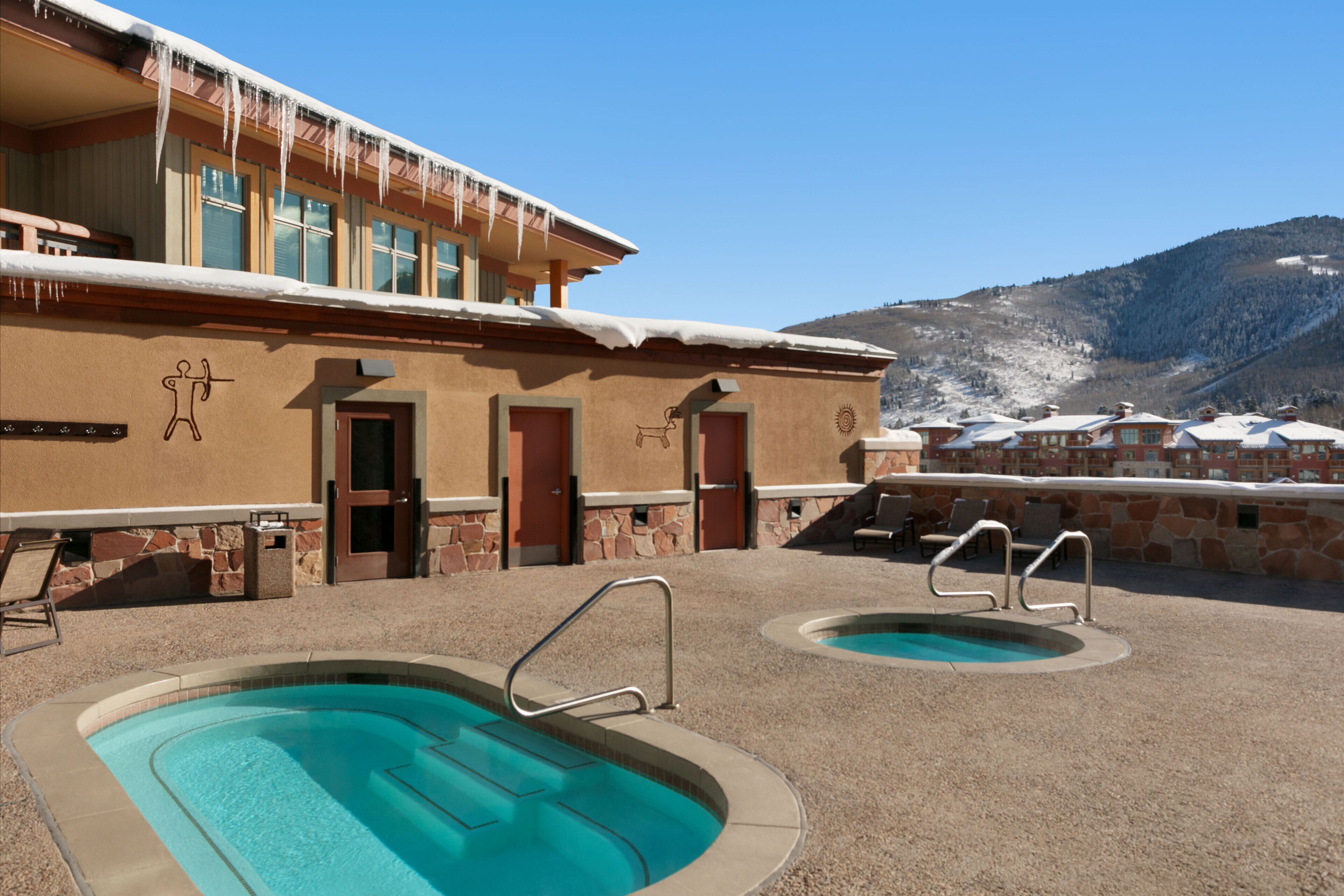 A pool area with two pools, a stone wall, and a building with a ski slope in the background.