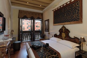 Una habitación de hotel con una cama, un escritorio con lámpara, una silla, un ventanal con vistas a edificios y una pared con diseño.