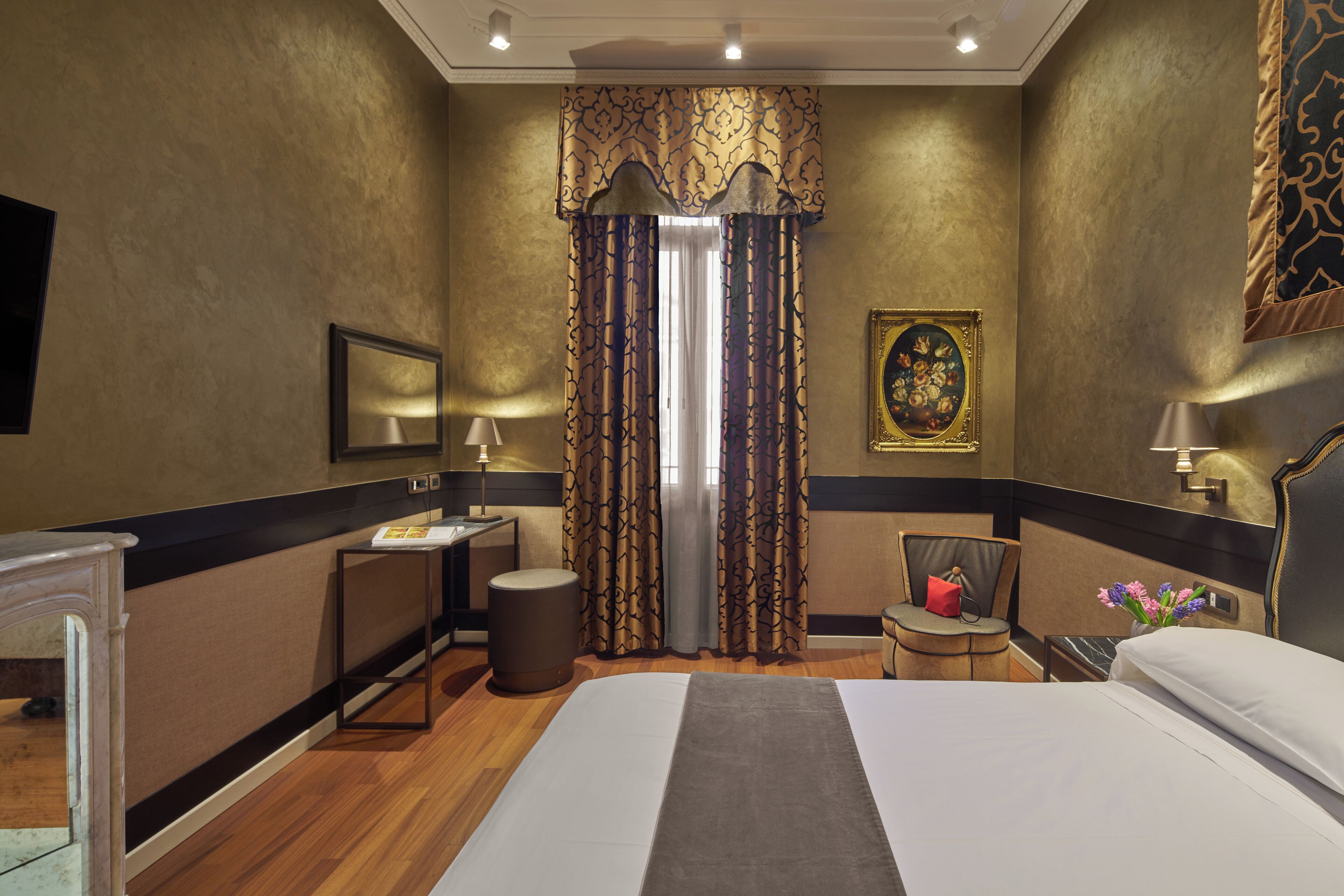 A hotel room with a large bed, a desk, a chair, a small table, a lamp, and a painting on the wall.