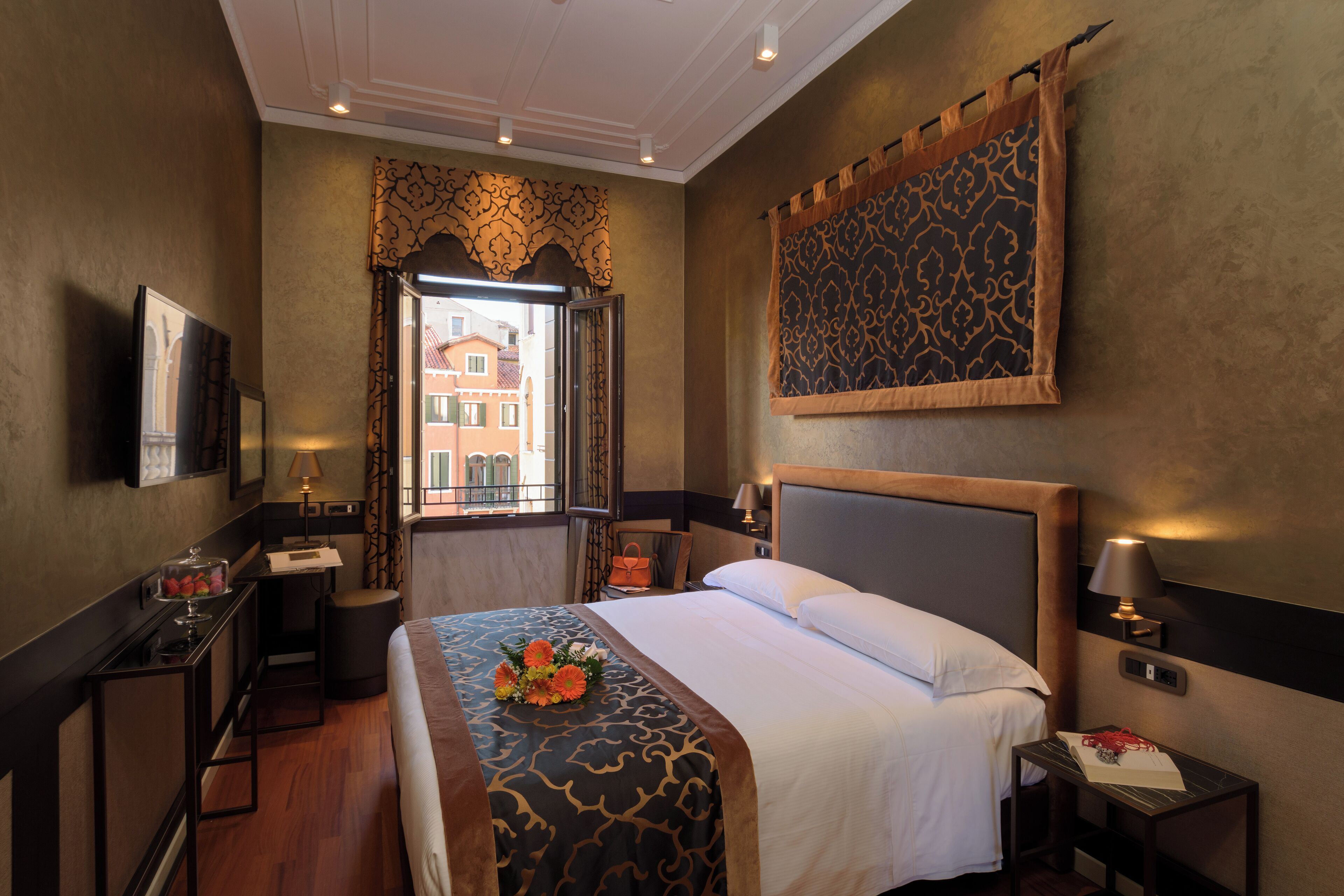 Une chambre d’hôtel avec un grand lit, un bureau, une chaise, une fenêtre donnant sur des immeubles et un téléviseur fixé au mur.
