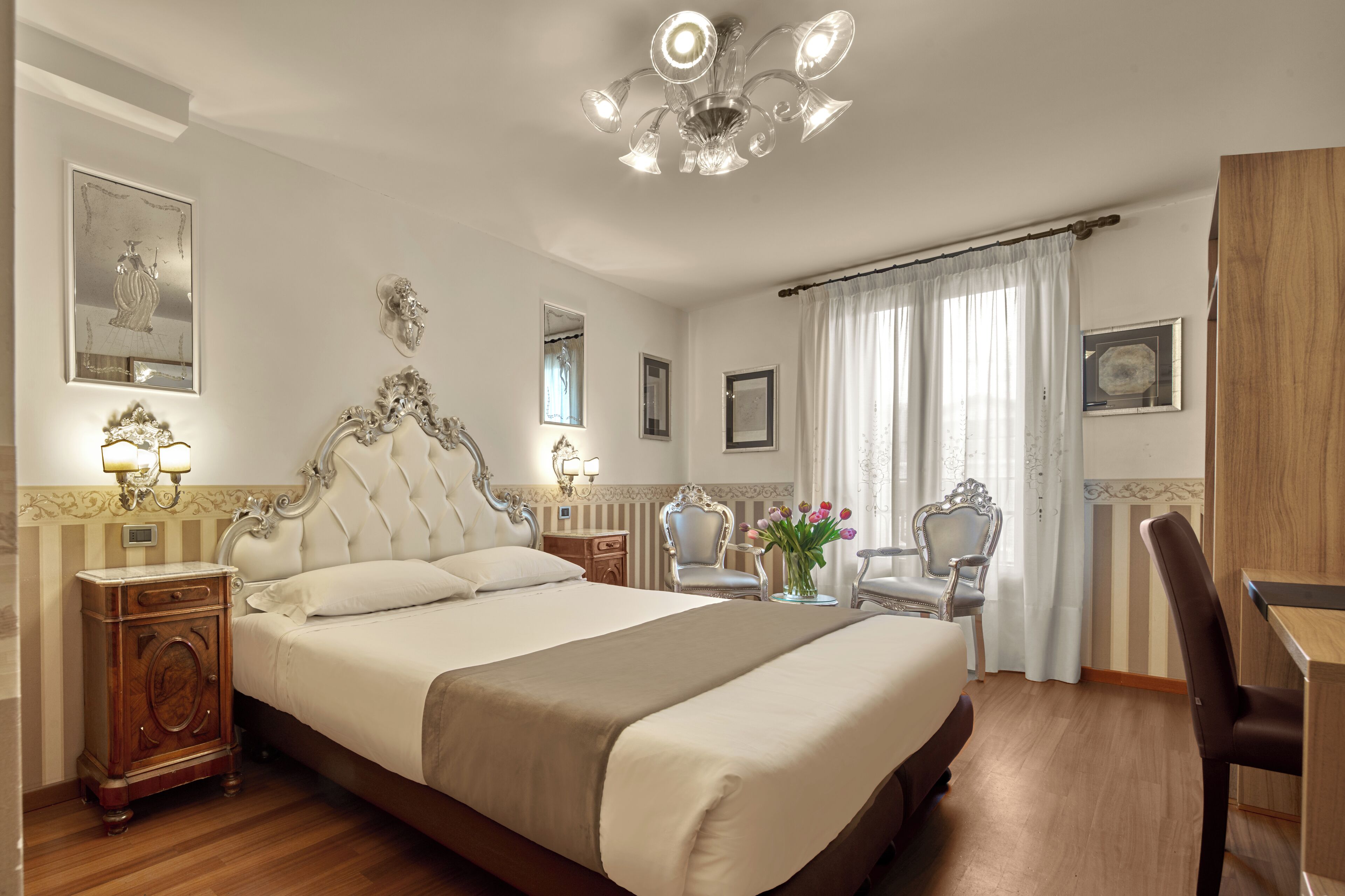 Ein Hotelzimmer mit einem großen Bett, einem Kronleuchter, einem Schreibtisch und einem Sessel.