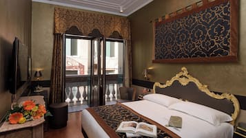 Quarto de hotel com uma cama grande, uma mesa com luminária, uma televisão e vista para a varanda externa.
