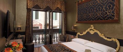 Habitación de hotel con una cama grande, un escritorio con lámpara, televisión y vista al balcón exterior.