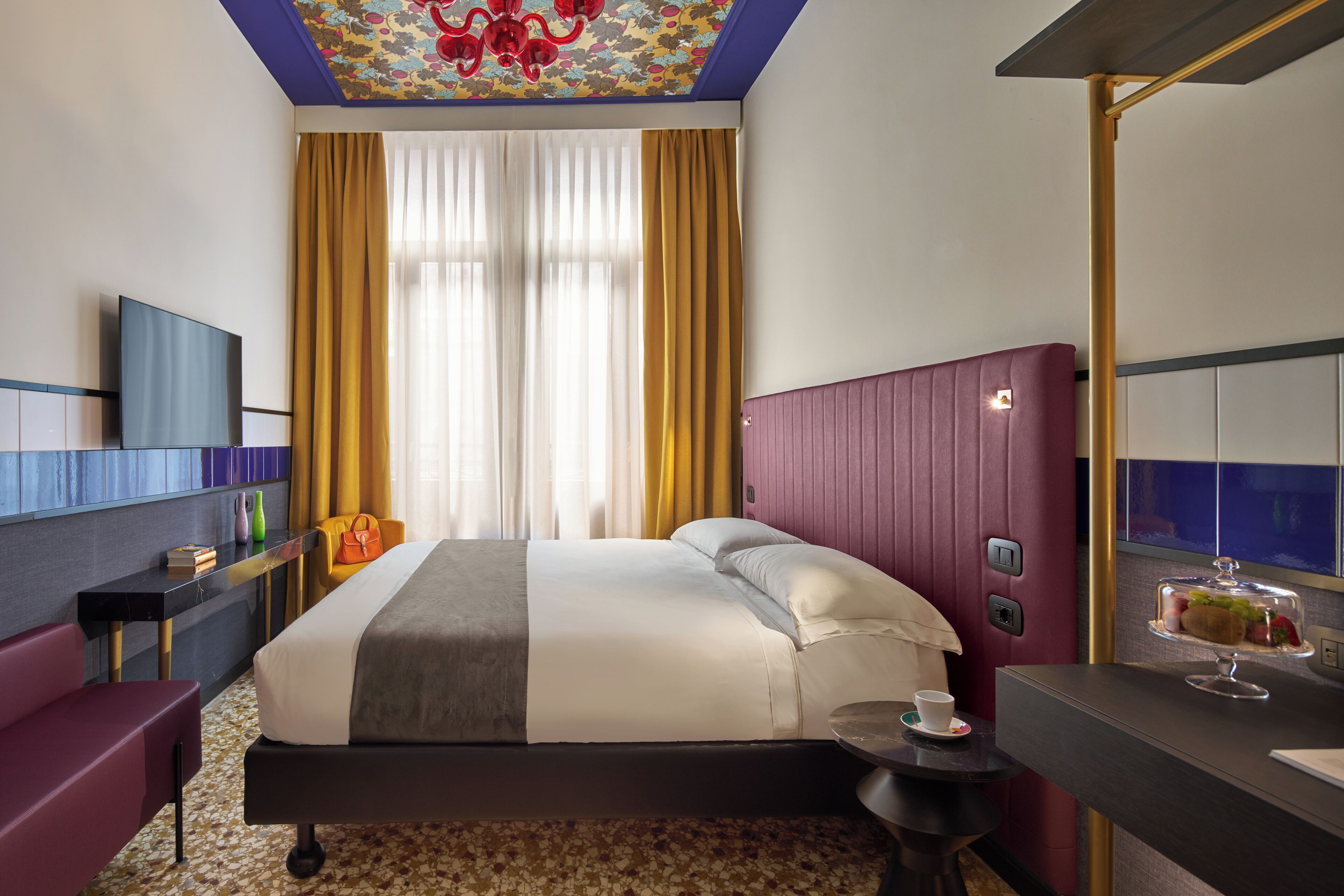 A hotel room with a bed, a desk, a chair, a TV, and a window with curtains.