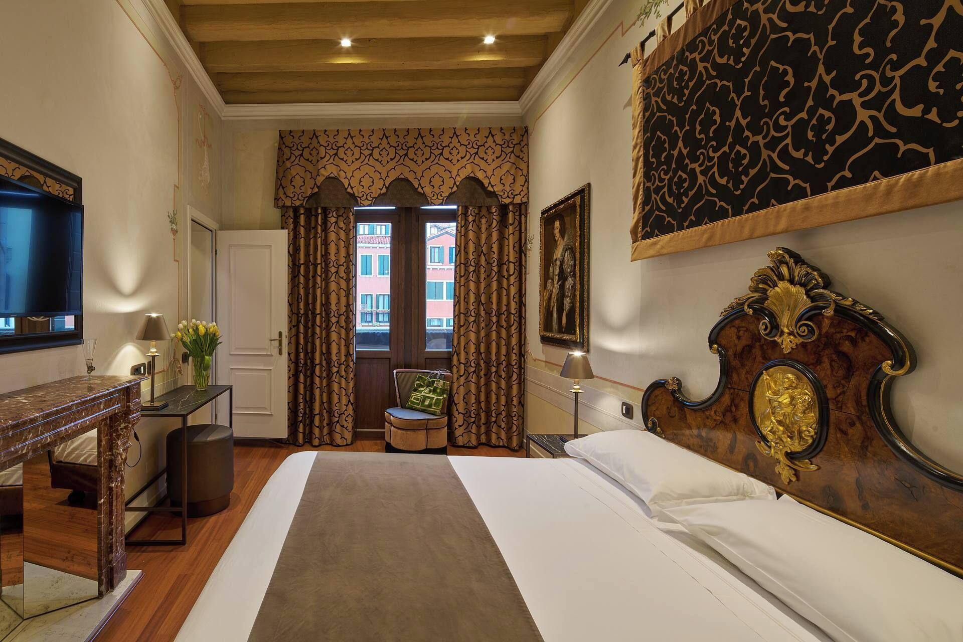 Habitación de hotel con cama, escritorio, silla, televisión y vistas al exterior.