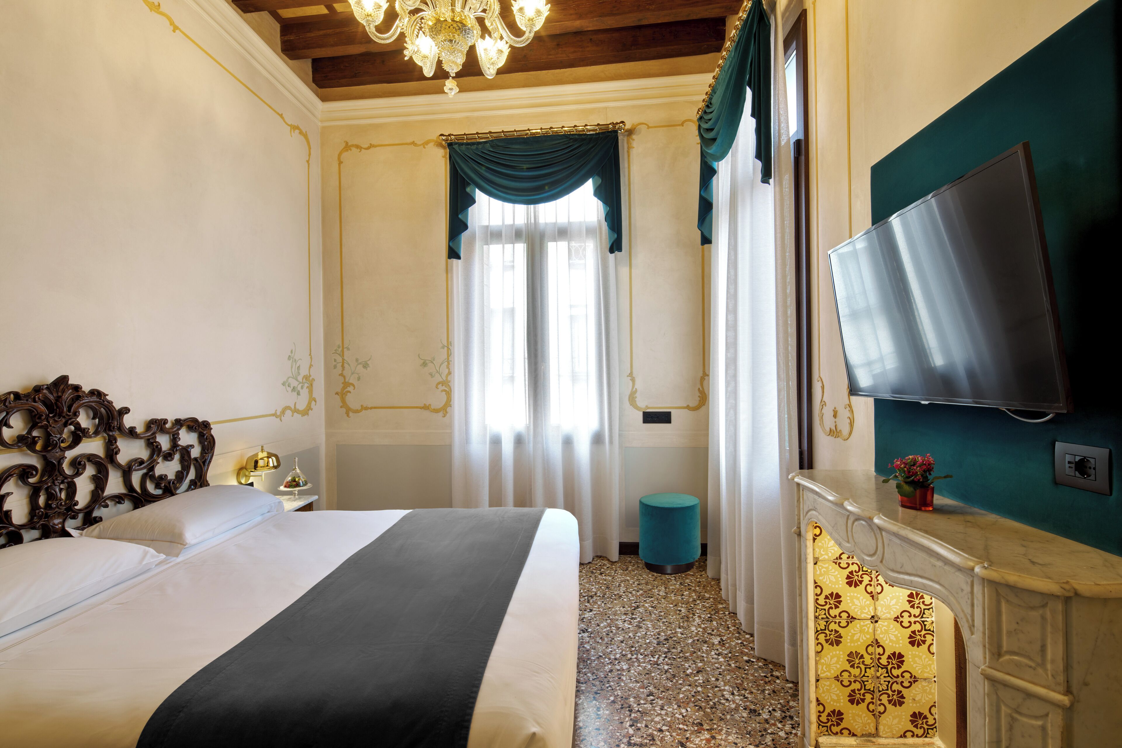 A hotel room with a large bed, a television mounted on the wall, a small round table, and a decorative mirror.