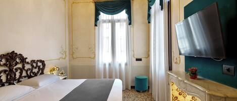 A hotel room with a large bed, a television mounted on the wall, a small round table, and a decorative mirror.