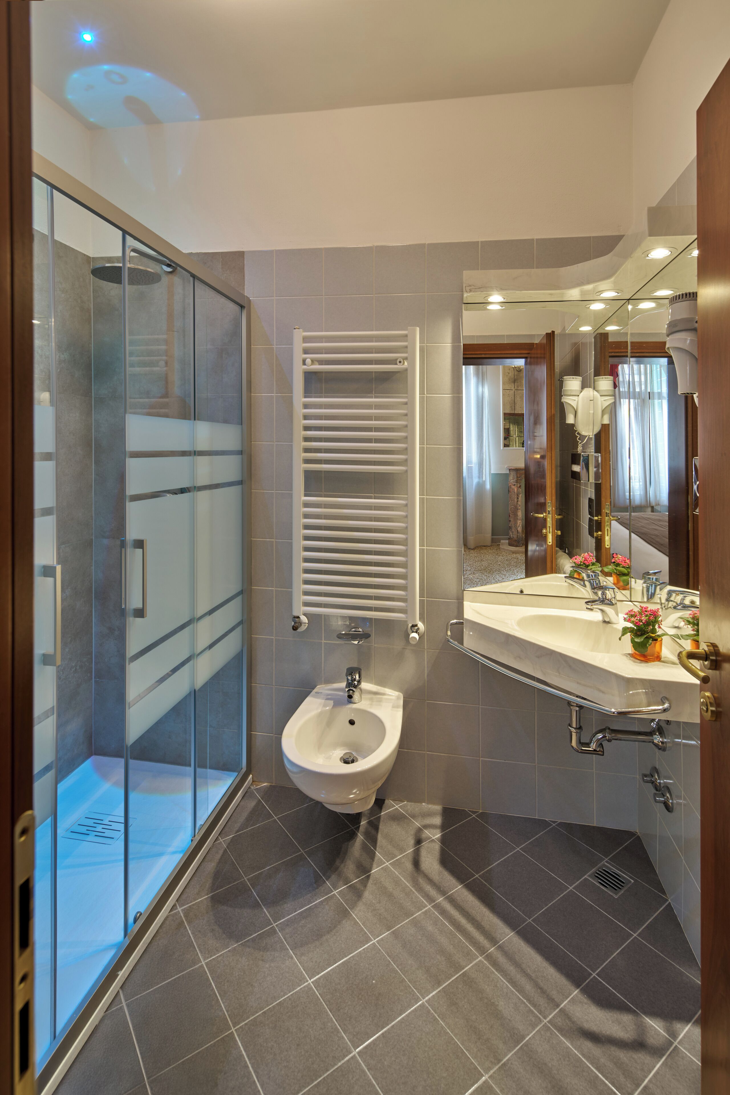 Un bagno moderno con cabina doccia in vetro, lavabo su piedistallo e uno specchio grande.