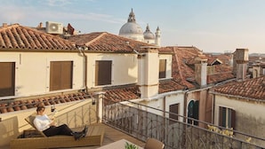 A rooftop terrace with a table and chairs, a potted plant, and a view of historic buildings with domed roofs. - Unahotels Ala Venezia - Adults Only (Venice)