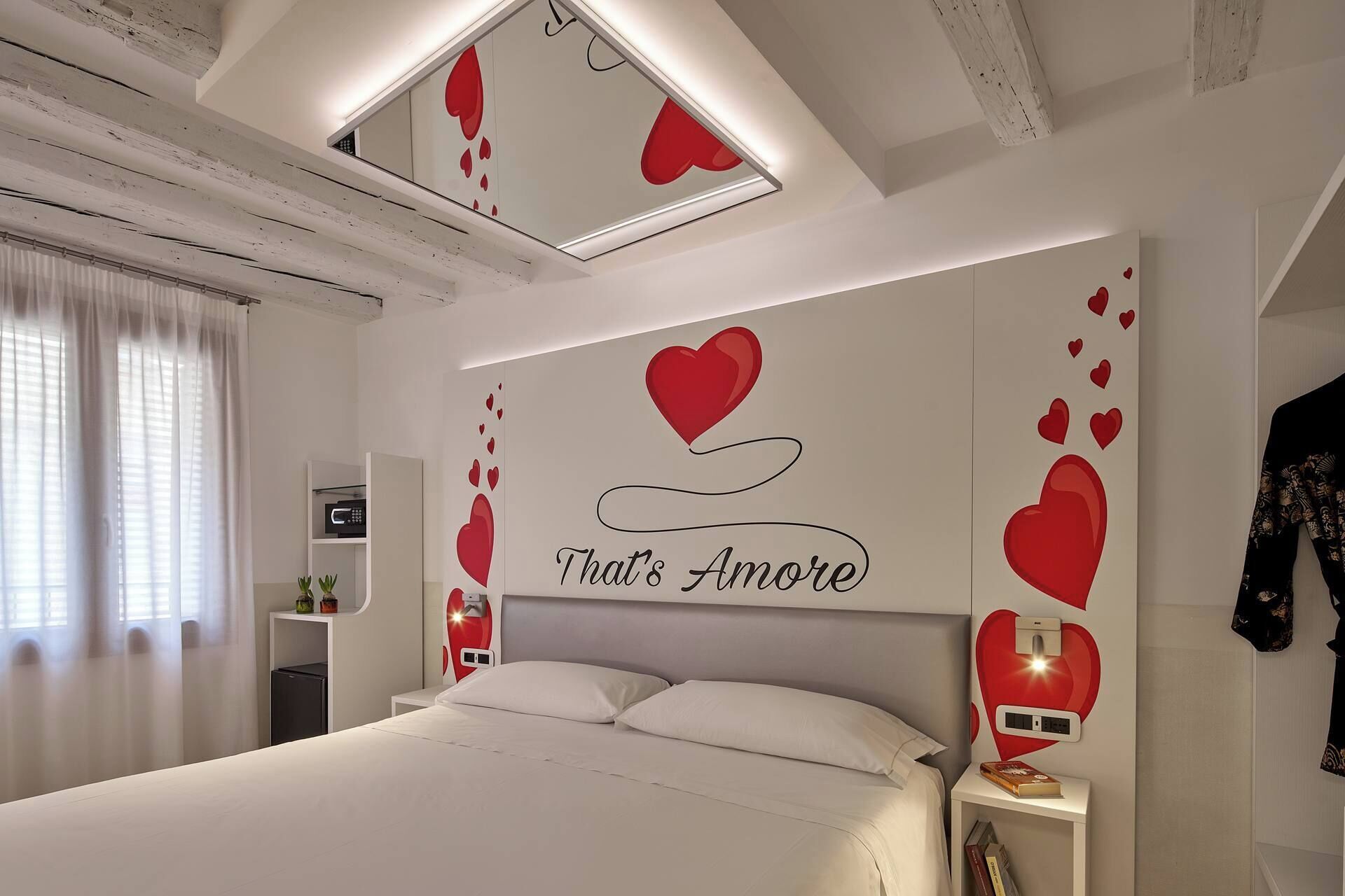Een slaapkamer met een bed, nachtkastjes, een spiegel en een wand met hartdecoraties.