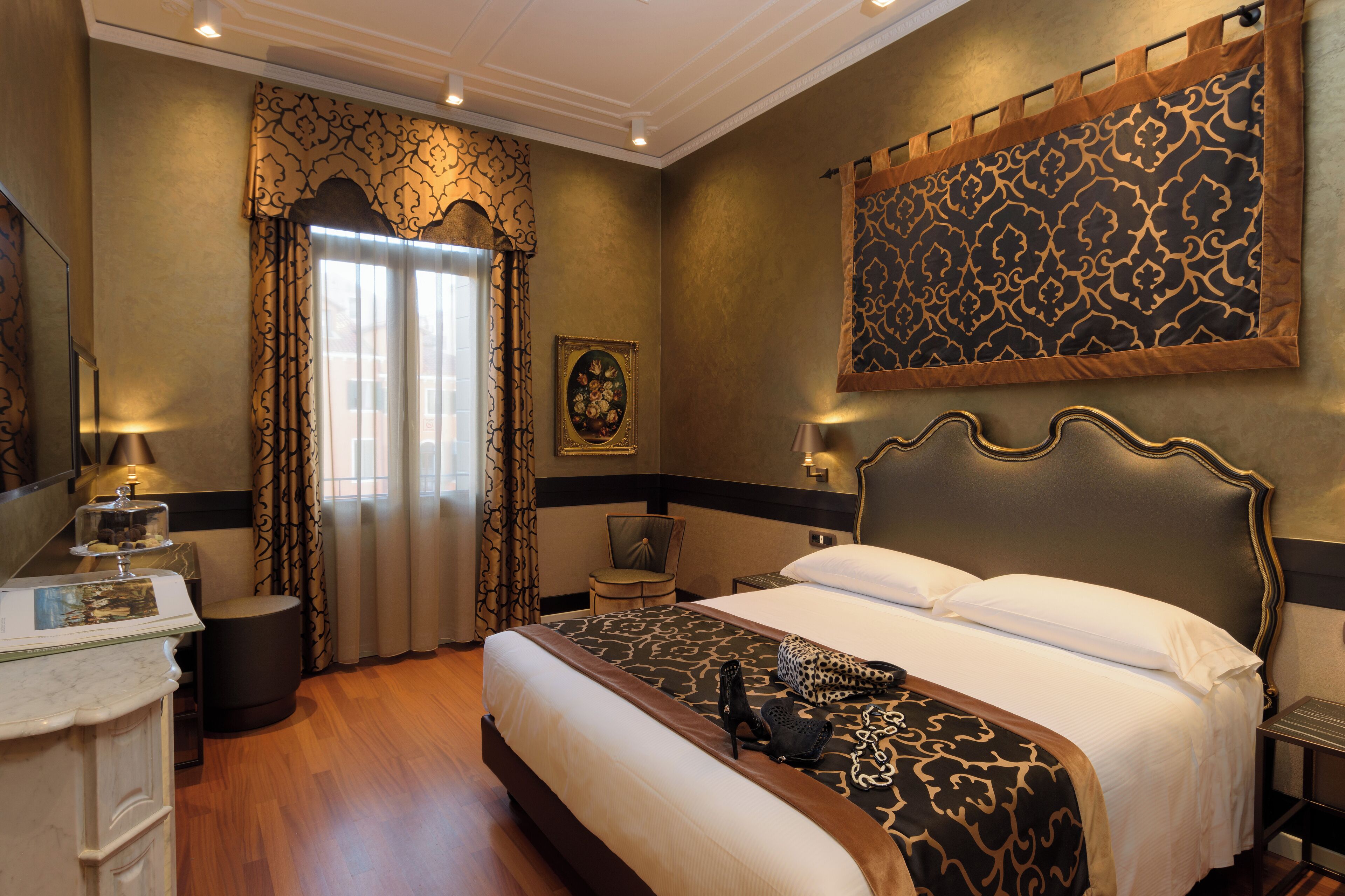 A hotel room with a large bed, a desk with a lamp, a chair, and a painting on the wall.