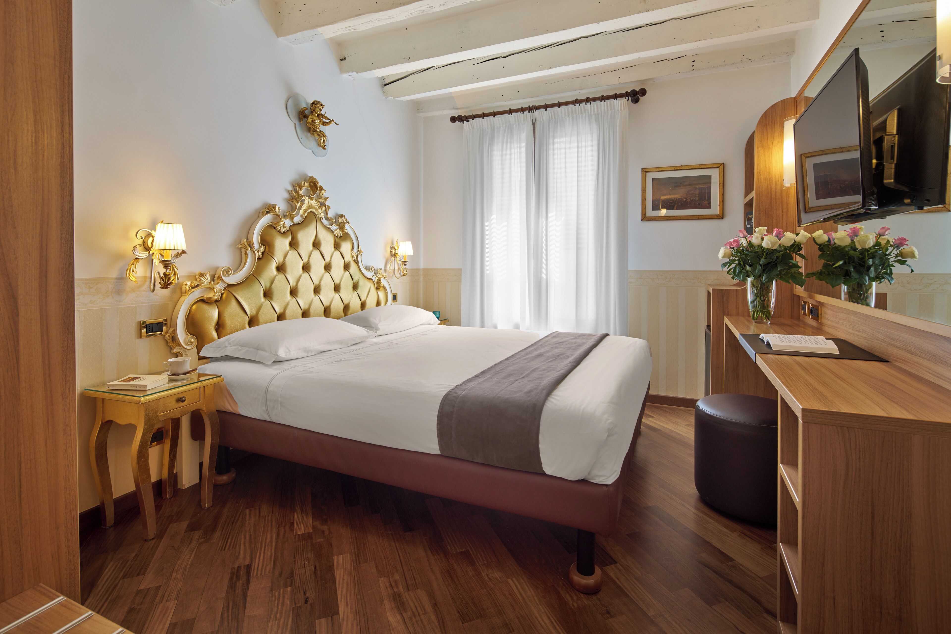 A hotel room with a large bed, wooden floor, a vanity with a mirror, and a window with curtains.