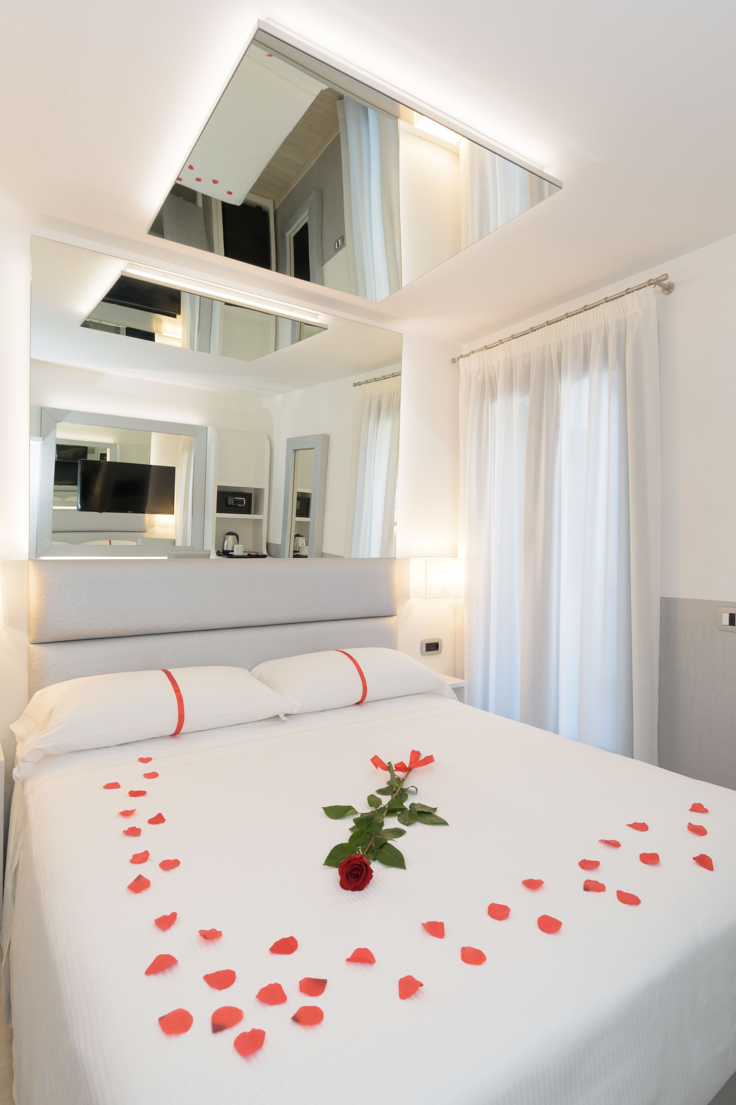 A modern hotel room with a large bed, a mirror, a TV, and a bathroom visible in the background.