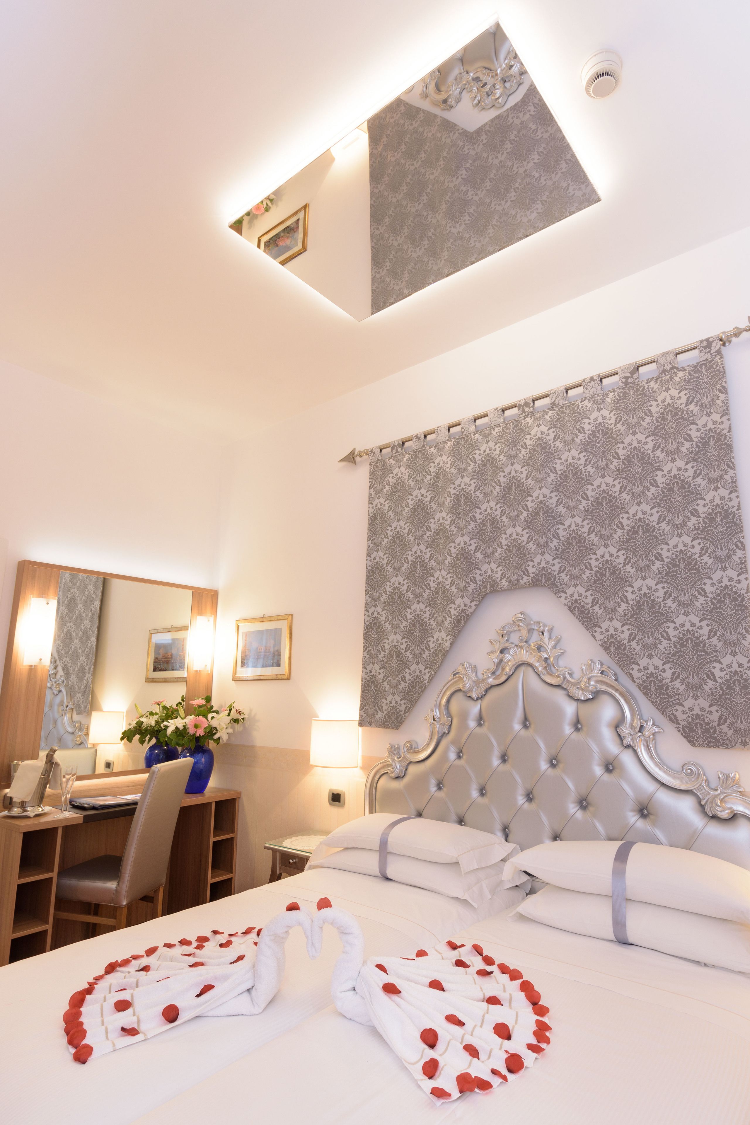 A hotel room with a bed, a desk, and a chair. There is a window with a view of the sky.