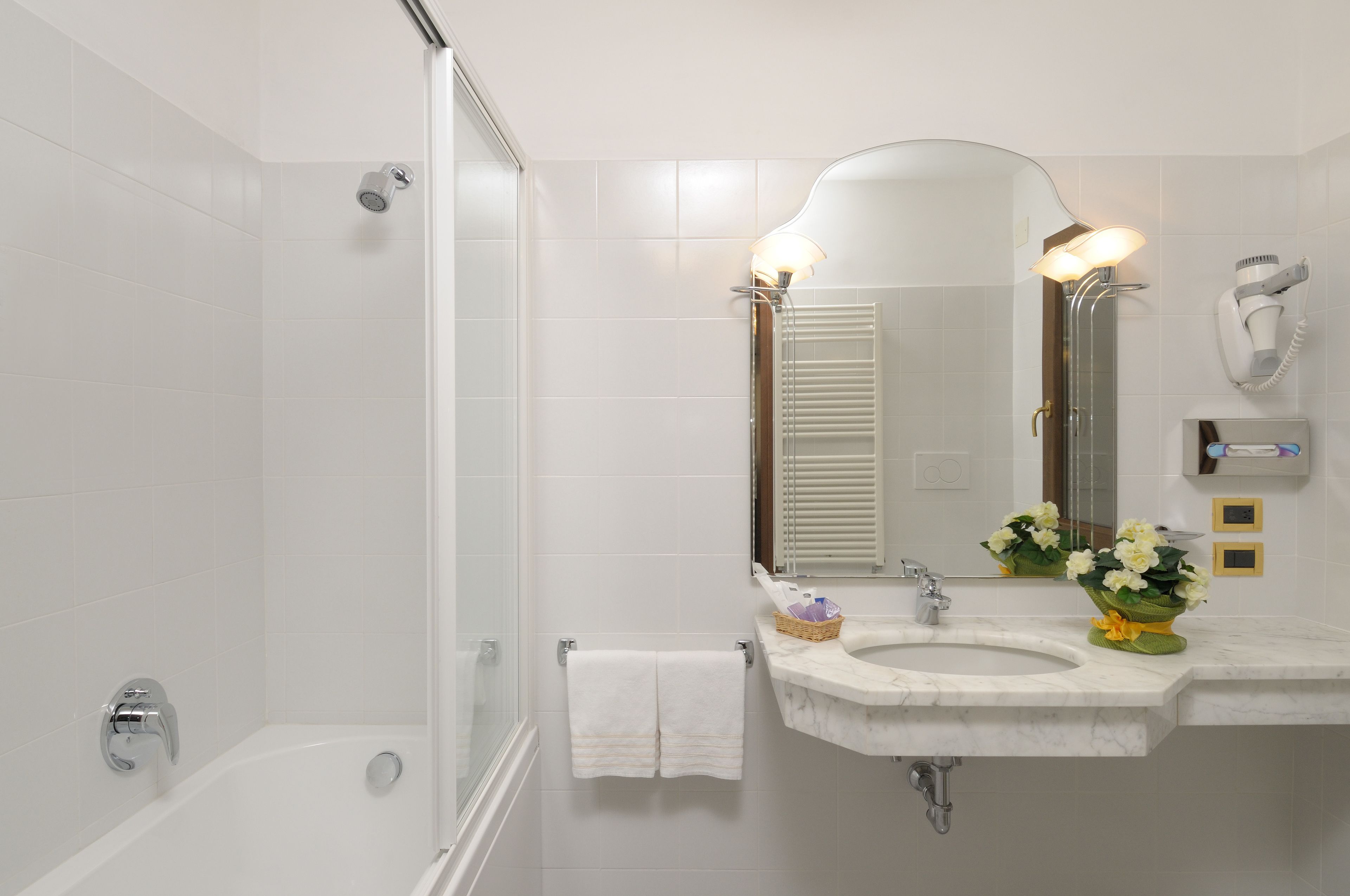 A bathroom with a bathtub, a sink with a mirror, a towel rack, and a hairdryer mounted on the wall.