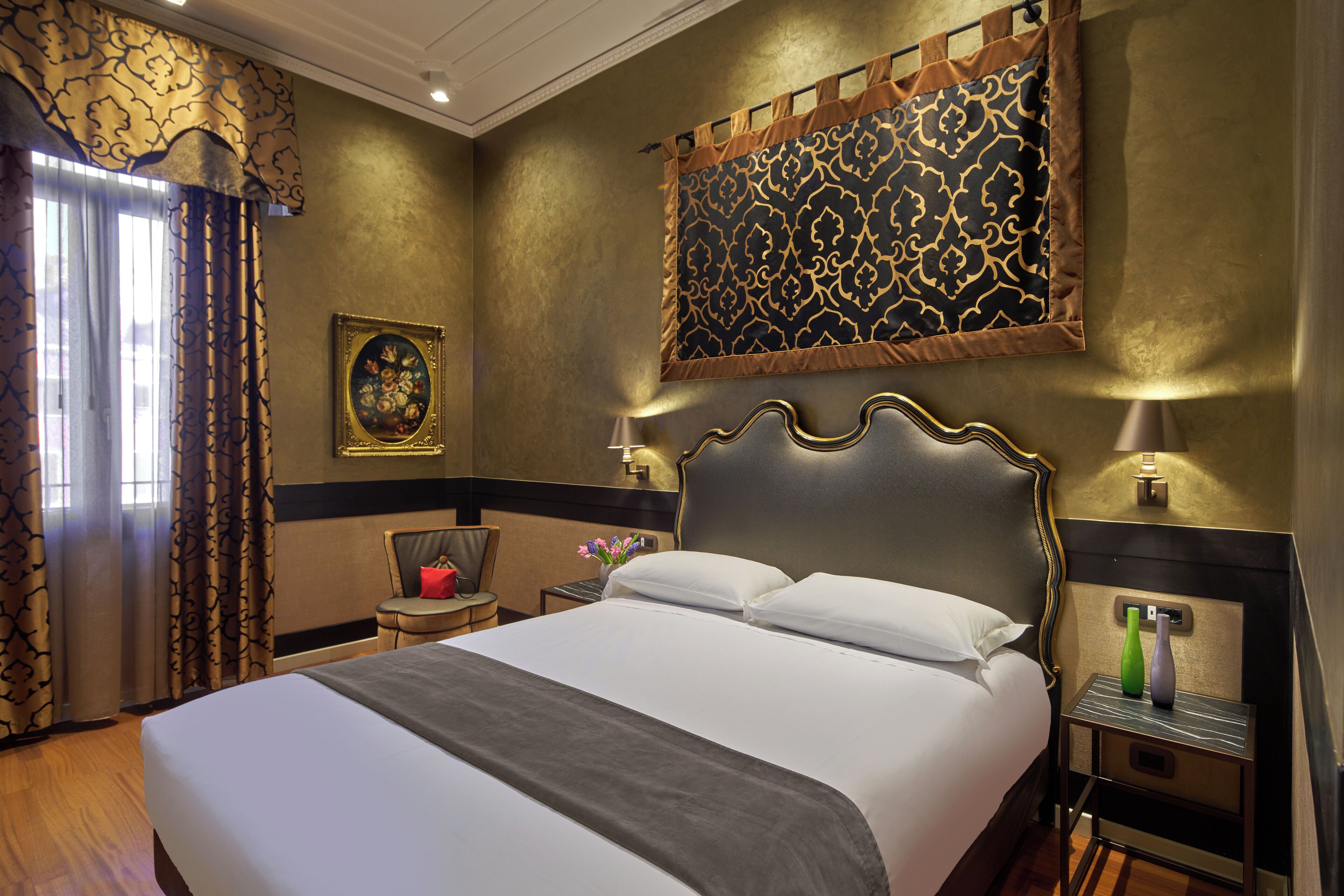 Une chambre d’hôtel avec un grand lit, une table de chevet avec une lampe, une chaise et un élément décoratif mural.