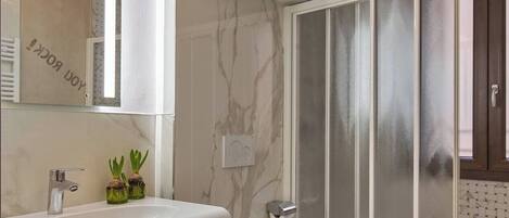 A modern bathroom with a marble vanity, a toilet, and a glass shower enclosure.
