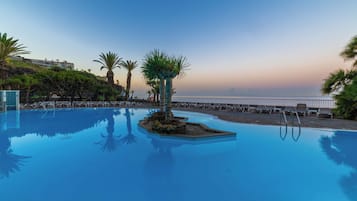 A pool with a small island, palm trees, and lounge chairs.
