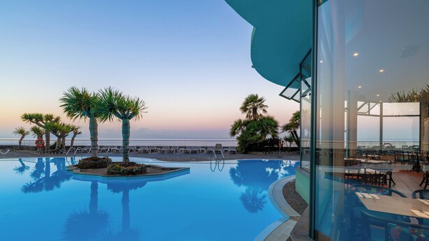 A swimming pool with palm trees and a view of the sea. - Pestana Ocean Bay Resort (Funchal)