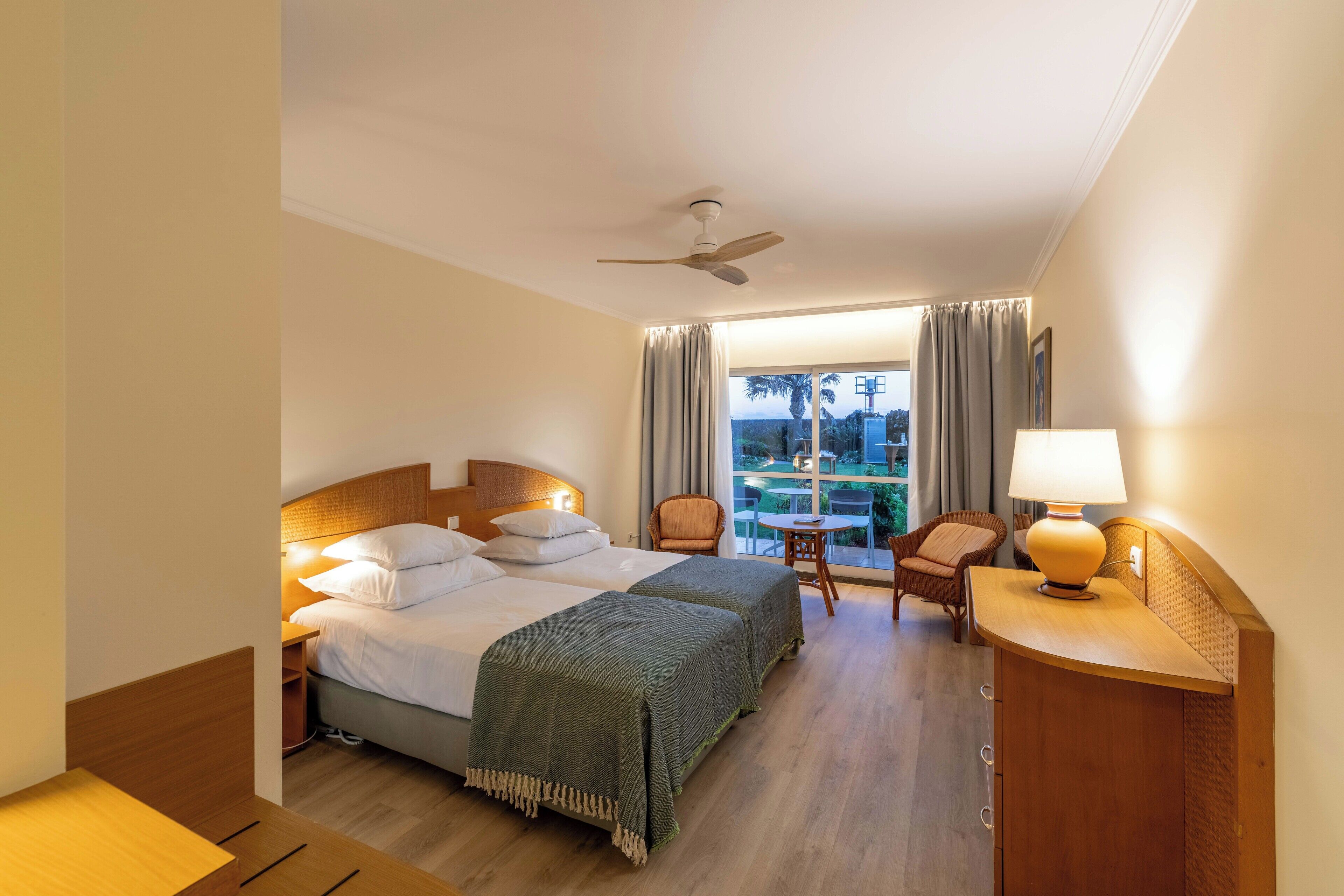 A hotel room with two beds, a desk, a chair, a table, and a view of the outdoors.