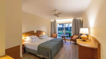 A hotel room with two beds, a desk, a chair, a table, and a view of the outdoors.