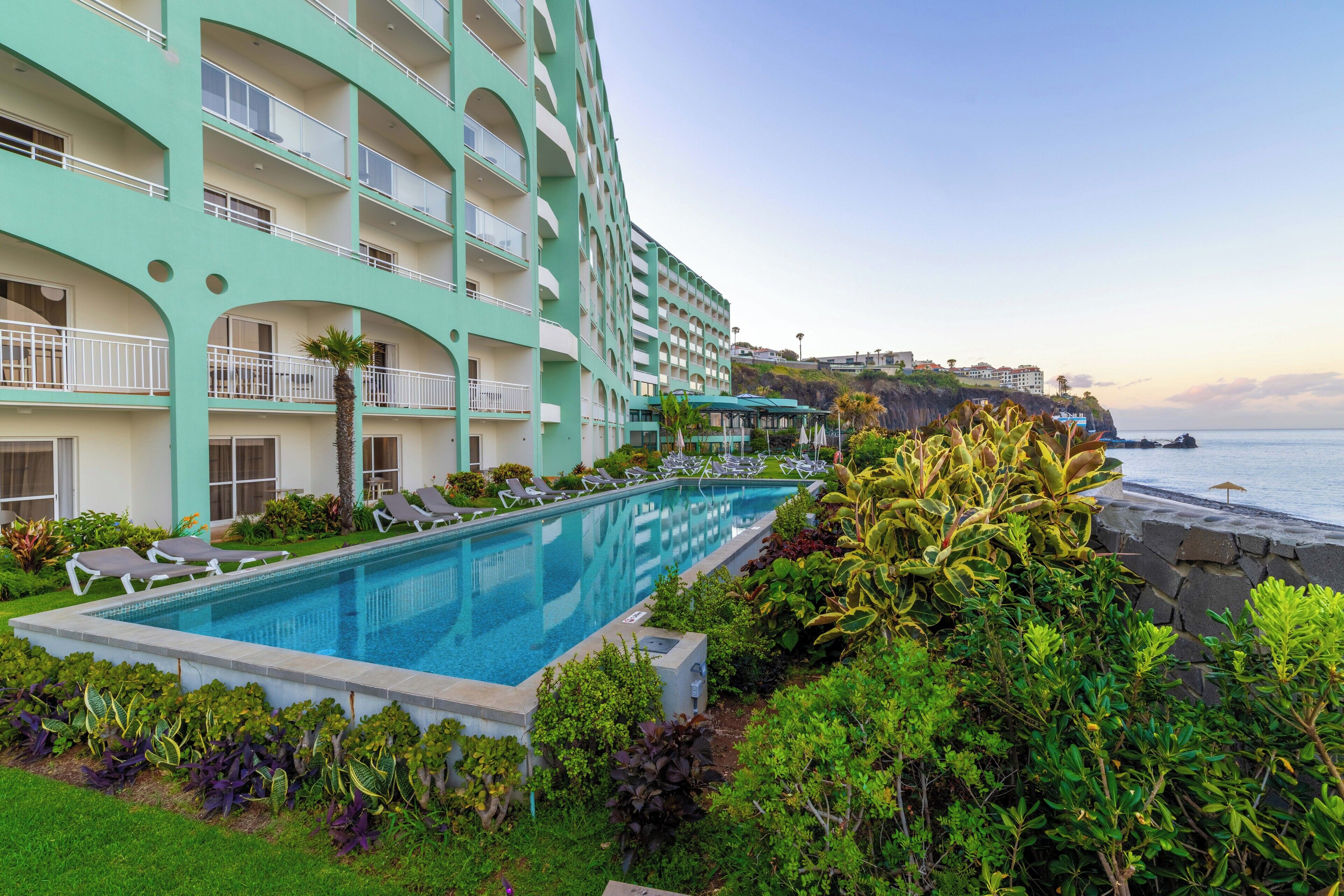 Un hôtel doté d’une piscine, entouré d’une végétation luxuriante et offrant une vue sur l’océan.