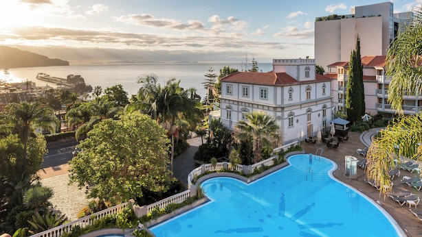 Hotel com piscina, vista para o mar e um edifício grande com telhado vermelho.