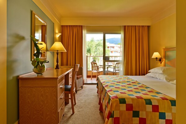 Habitación de hotel con cama, escritorio, silla, lámpara, espejo y vista al exterior.