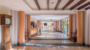 Um hall de hotel espaçoso, com teto alto, grandes colunas e um balcão de recepção central.