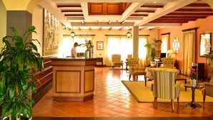 A lobby with a reception desk, seating area, and a large painting on the wall. - Pestana Village Garden Hotel (Funchal)
