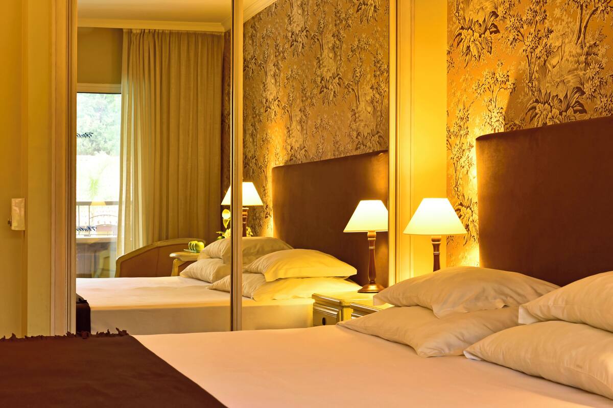 Une chambre d’hôtel avec un grand lit, deux lampes de chevet et un miroir qui reflète la pièce.